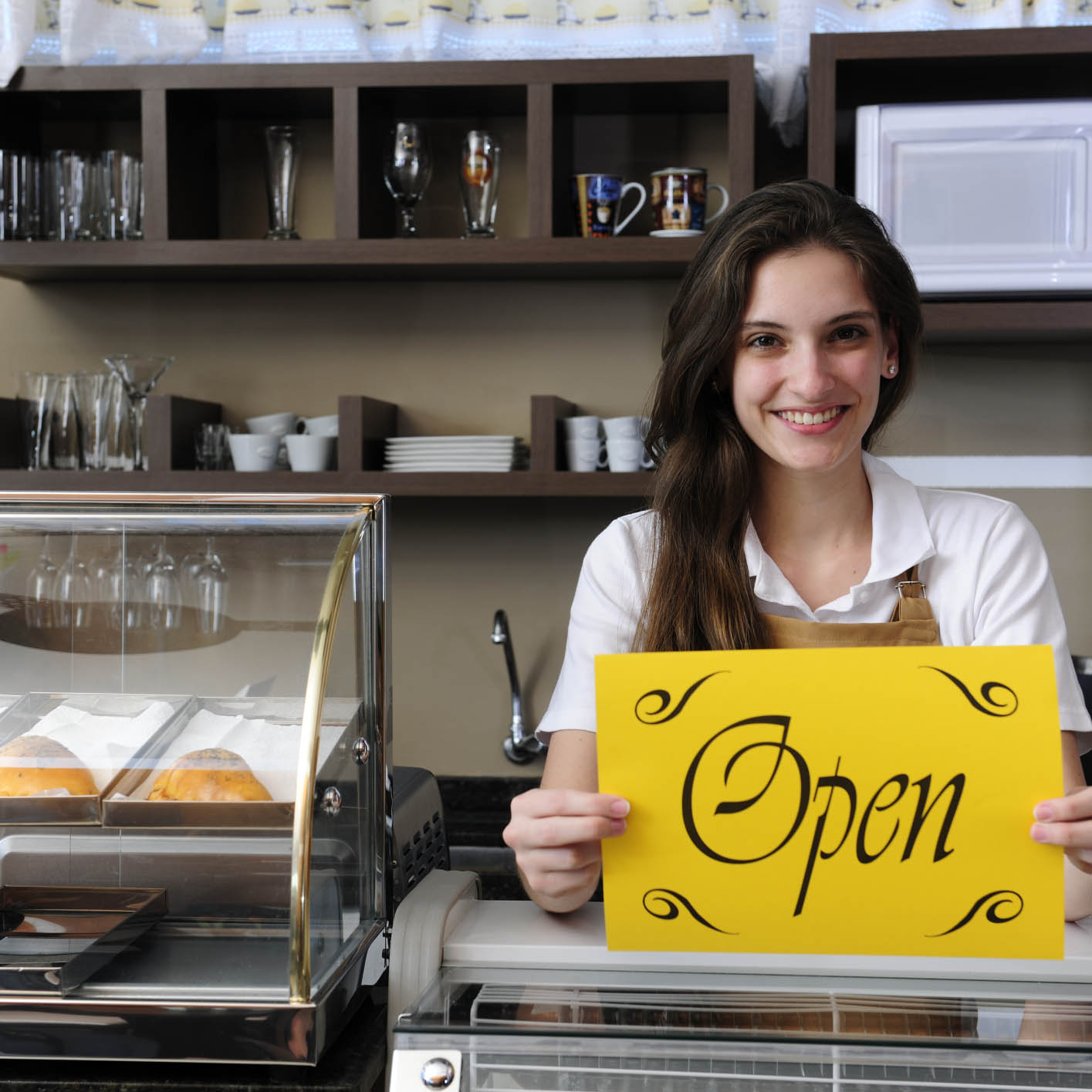 young woman in bakery holding sign saying Open!
