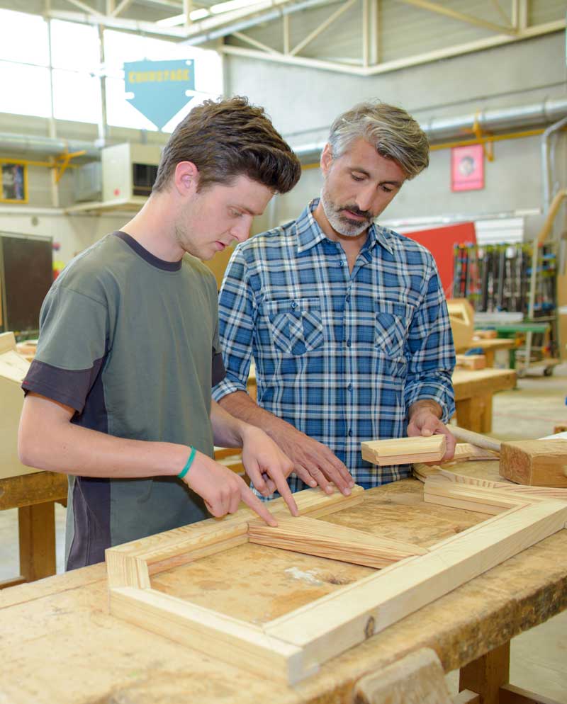 Teen working beside mentor on carpentry project.