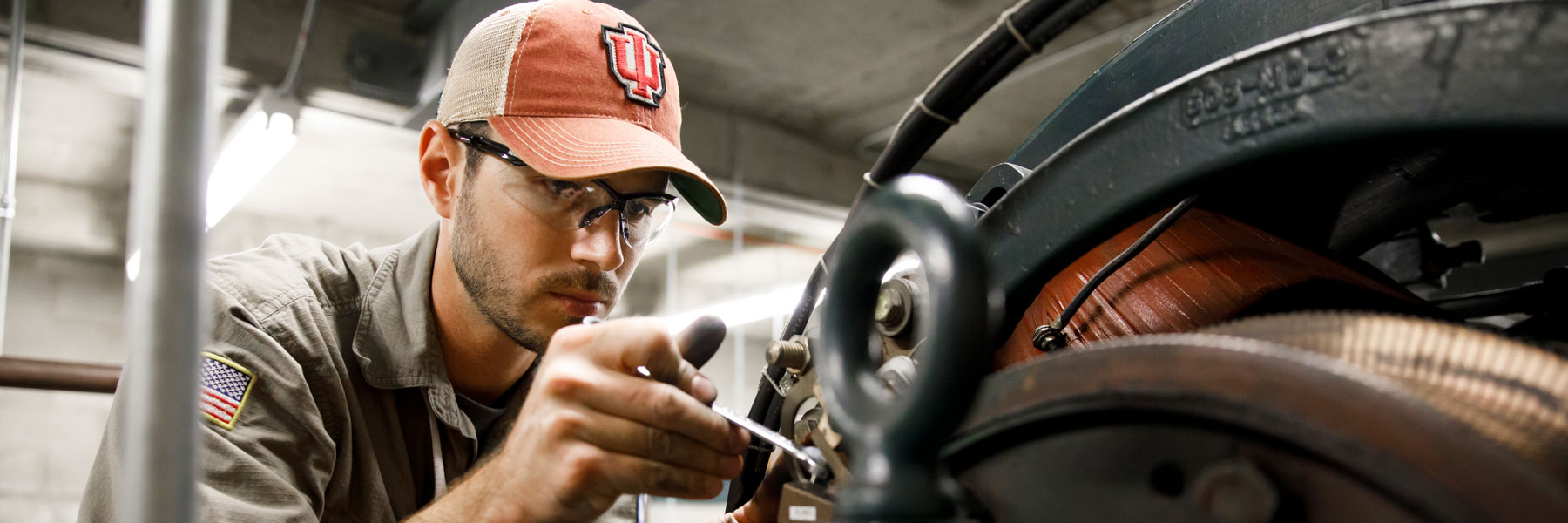 Young worker wearing IU cap uses tools in machine shop.