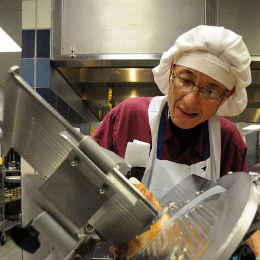 Woman wearing hairnet using meat slicer.