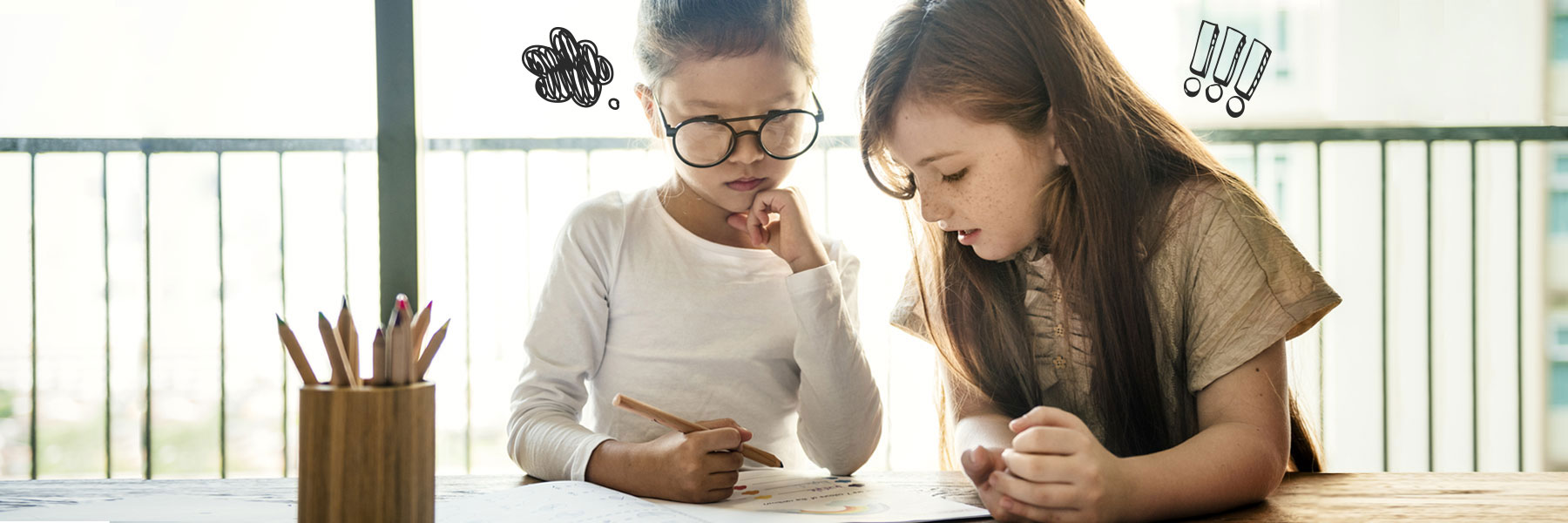 Two young girls sitting together at table with pencils looking at a specific piece of paper with serious thinking expressions on the faces. 