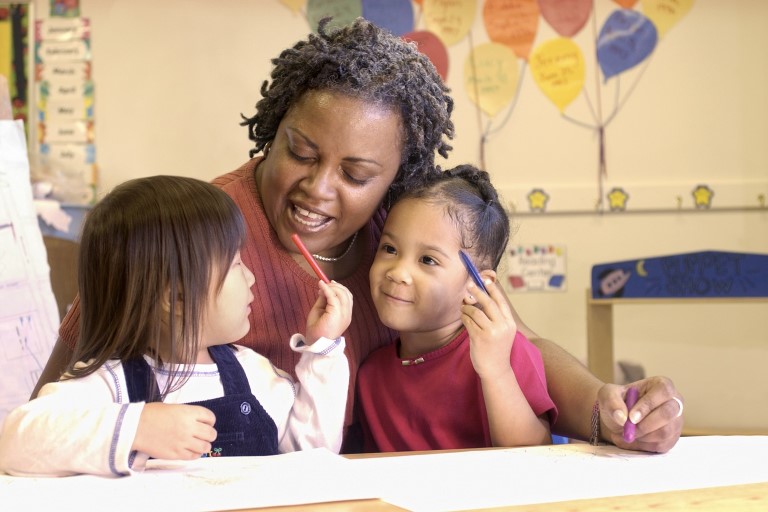 A preschool teacher talking with two students.